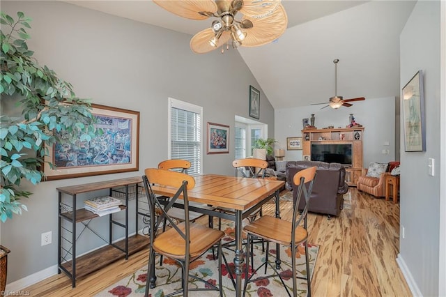 dining space featuring a tiled fireplace, ceiling fan, high vaulted ceiling, and light wood-type flooring