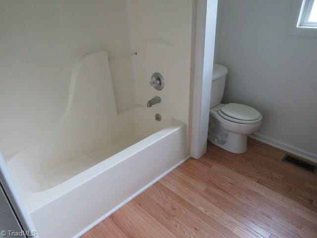 bathroom with toilet, shower / washtub combination, and hardwood / wood-style floors