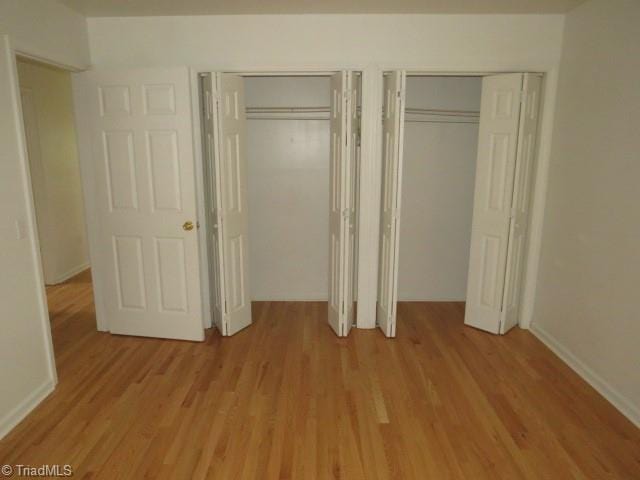 unfurnished bedroom featuring light hardwood / wood-style flooring and multiple closets