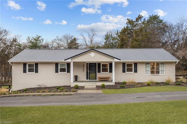 ranch-style home featuring a front yard, covered porch, brick siding, and metal roof