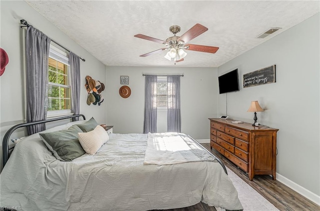 bedroom featuring baseboards, a textured ceiling, visible vents, ceiling fan, and wood finished floors