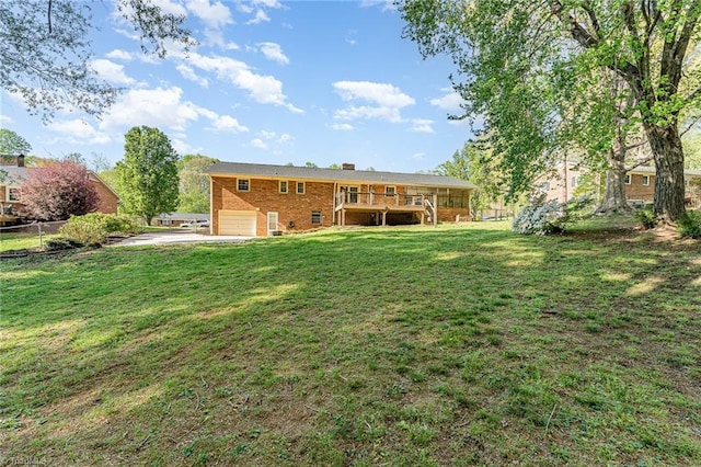 view of yard with a garage, driveway, a wooden deck, and fence