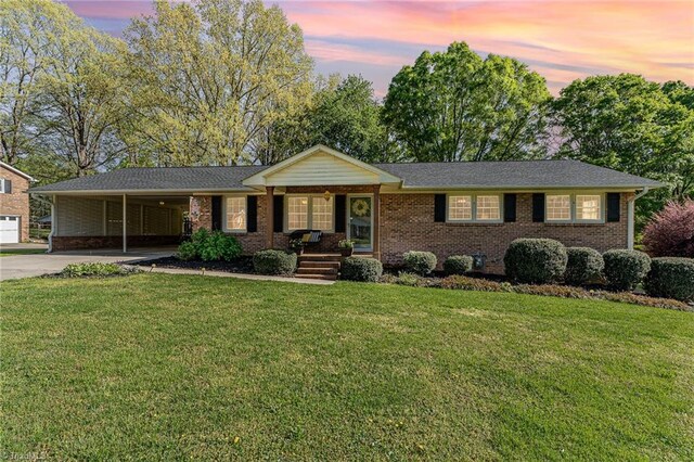 ranch-style home with brick siding, driveway, an attached carport, and a lawn