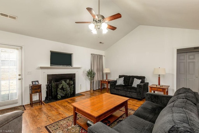 living room featuring a fireplace, lofted ceiling, visible vents, ceiling fan, and wood finished floors