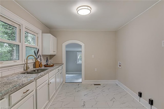 kitchen featuring light stone countertops, ornamental molding, sink, and white cabinets