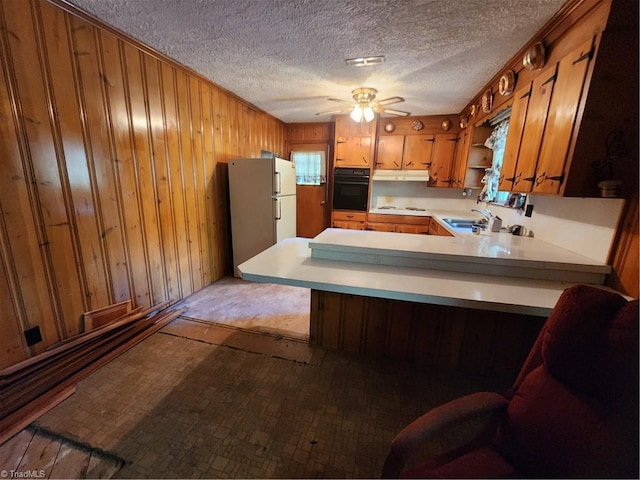 kitchen with wooden walls, oven, white fridge, kitchen peninsula, and a textured ceiling