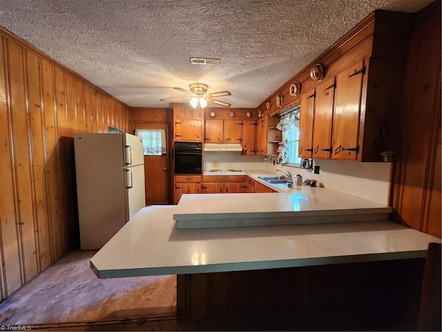 kitchen featuring white appliances, ceiling fan, a textured ceiling, kitchen peninsula, and wood walls