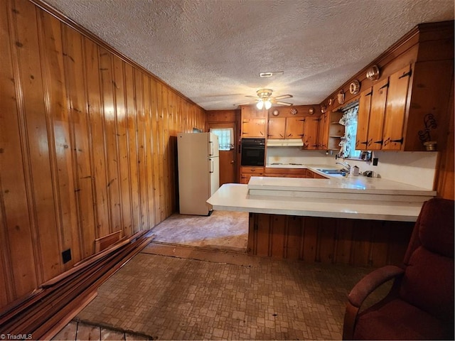 kitchen with sink, wood walls, white refrigerator, kitchen peninsula, and oven