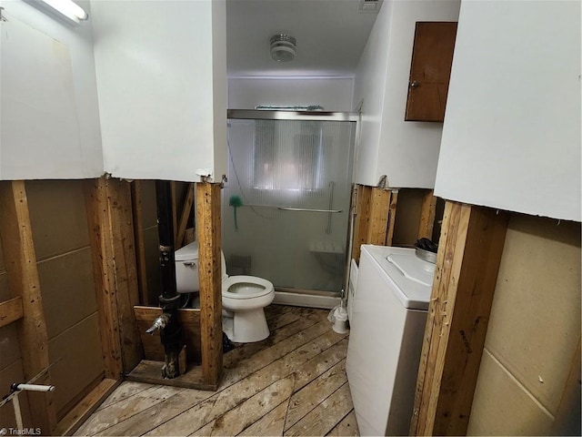 bathroom with hardwood / wood-style flooring, vanity, washer / dryer, a shower with shower door, and toilet