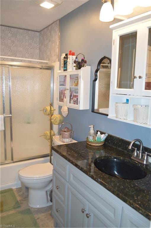 full bathroom with enclosed tub / shower combo, vanity, and toilet