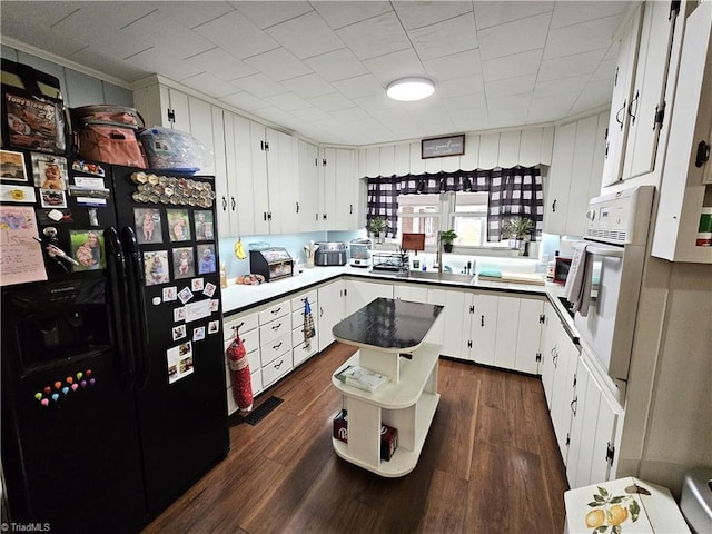 kitchen with black fridge, white cabinetry, dark hardwood / wood-style floors, and oven