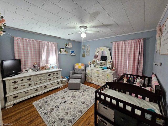 bedroom featuring ceiling fan, dark hardwood / wood-style flooring, and a crib