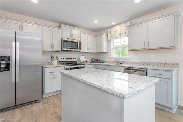 kitchen featuring stainless steel appliances, light stone countertops, a kitchen island, and light hardwood / wood-style flooring