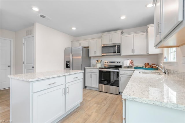 kitchen featuring sink, stainless steel appliances, a center island, white cabinets, and light wood-type flooring