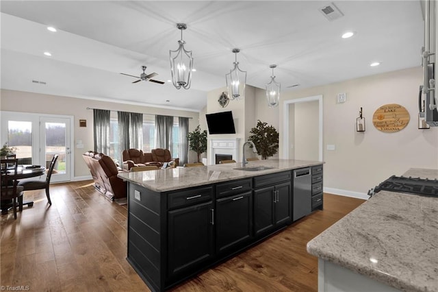 kitchen with ceiling fan, light stone countertops, dark hardwood / wood-style flooring, decorative light fixtures, and a center island with sink