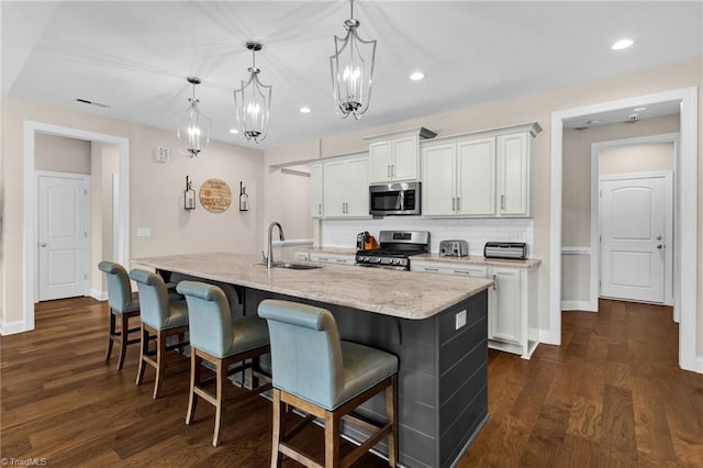 kitchen featuring hanging light fixtures, stainless steel appliances, an island with sink, a kitchen bar, and white cabinets