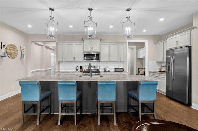 kitchen featuring hanging light fixtures, appliances with stainless steel finishes, a large island, white cabinetry, and a breakfast bar area