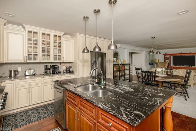 kitchen featuring sink, hanging light fixtures, appliances with stainless steel finishes, an island with sink, and dark stone counters