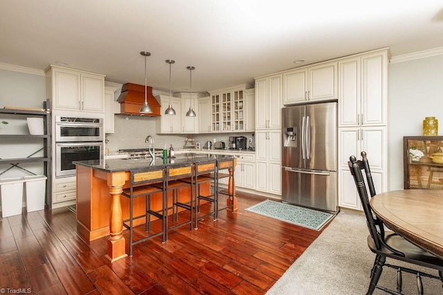 kitchen with premium range hood, a kitchen bar, a center island with sink, appliances with stainless steel finishes, and pendant lighting