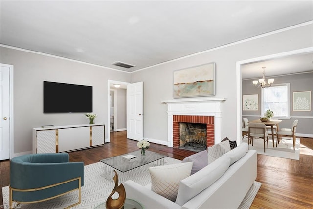 living room with hardwood / wood-style flooring, an inviting chandelier, a brick fireplace, and crown molding