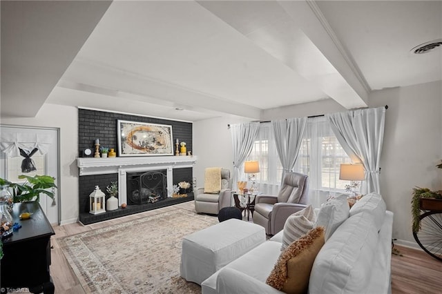 living area featuring beam ceiling, a brick fireplace, wood finished floors, and baseboards