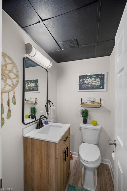 half bathroom with visible vents, toilet, wood finished floors, baseboards, and vanity