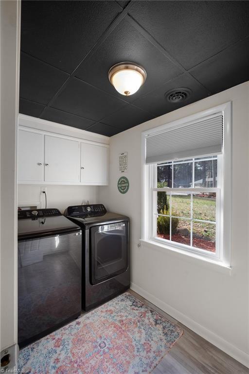 laundry area featuring wood finished floors, visible vents, baseboards, cabinet space, and independent washer and dryer