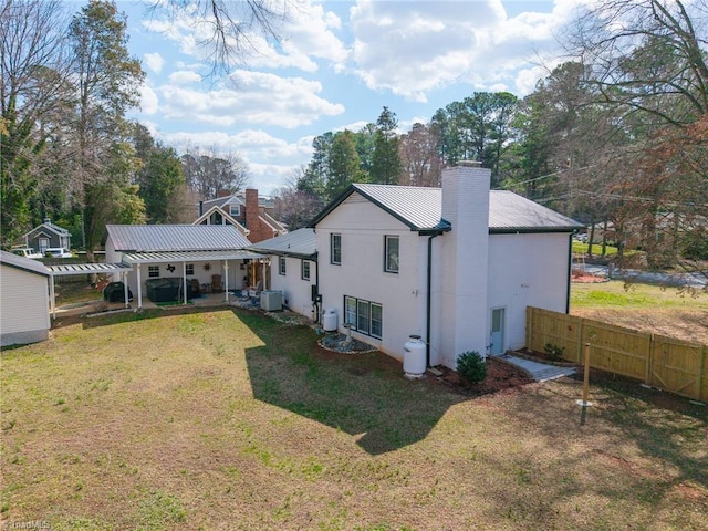 rear view of house featuring fence, central AC unit, a chimney, a lawn, and metal roof