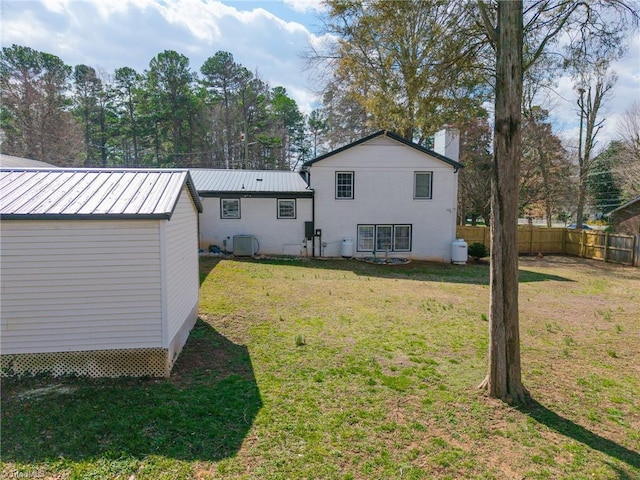 rear view of property with fence, a lawn, metal roof, a chimney, and a standing seam roof