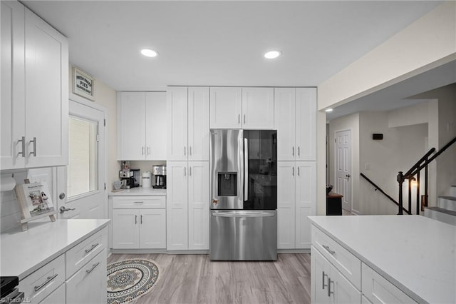 kitchen with recessed lighting, light countertops, light wood-style floors, stainless steel refrigerator with ice dispenser, and white cabinetry