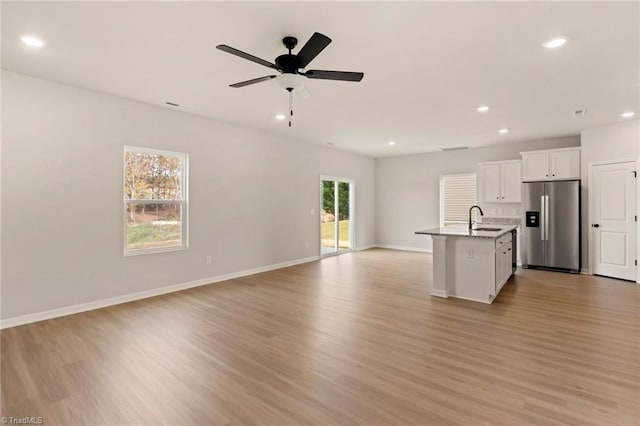 kitchen with sink, light hardwood / wood-style flooring, stainless steel fridge, a kitchen island with sink, and white cabinets