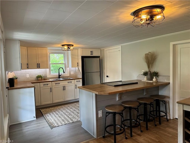 kitchen with a sink, wood counters, freestanding refrigerator, and a notable chandelier