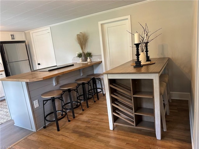 bar with crown molding, baseboards, freestanding refrigerator, and wood finished floors