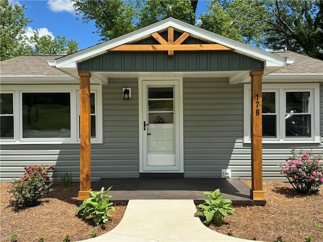view of exterior entry with board and batten siding, a shingled roof, and a porch