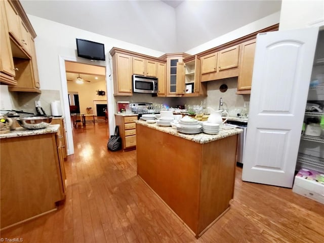 kitchen with light stone counters, light wood-type flooring, ceiling fan, and a kitchen island