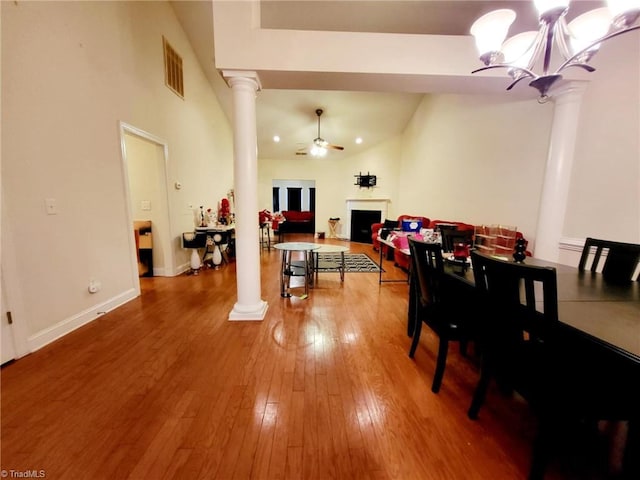 dining room with high vaulted ceiling, wood-type flooring, ceiling fan with notable chandelier, and ornate columns