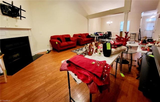 living room with hardwood / wood-style floors, a notable chandelier, vaulted ceiling, and decorative columns