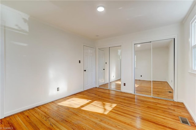 unfurnished bedroom with multiple closets and wood-type flooring