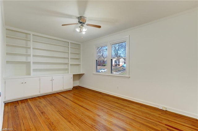 unfurnished room featuring built in desk, built in shelves, ceiling fan, light hardwood / wood-style flooring, and crown molding