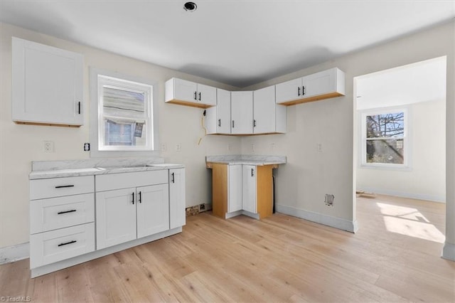 kitchen with sink, light stone counters, white cabinets, and light hardwood / wood-style floors