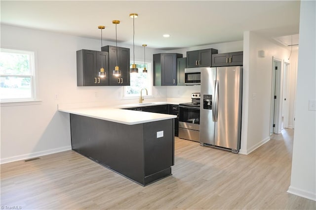 kitchen with stainless steel appliances, kitchen peninsula, sink, hanging light fixtures, and light hardwood / wood-style floors