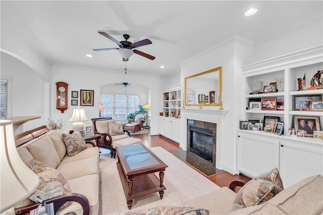 living room with ornamental molding, ceiling fan, built in features, a fireplace, and hardwood / wood-style floors