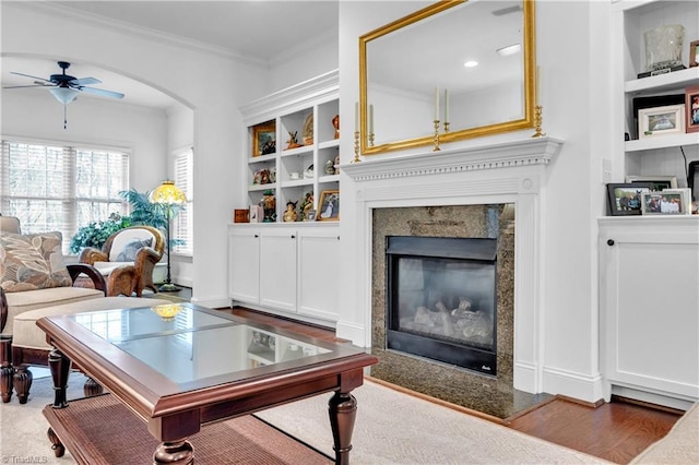 living room with a high end fireplace, built in shelves, ceiling fan, and hardwood / wood-style floors