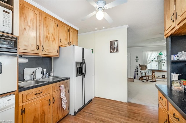 kitchen with dark countertops, crown molding, light wood-style floors, white appliances, and a sink