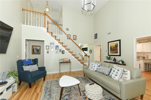 living room with a towering ceiling, stairs, light wood finished floors, and baseboards