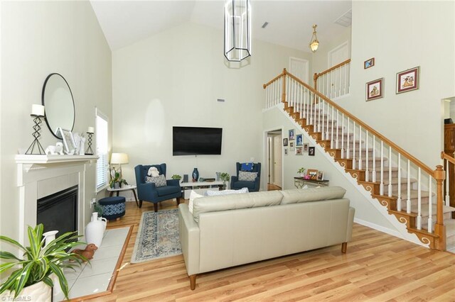 living room featuring high vaulted ceiling, stairs, a glass covered fireplace, wood finished floors, and baseboards