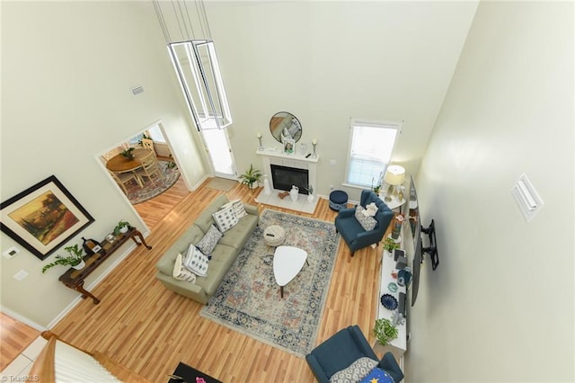 living room with a high ceiling, wood finished floors, a glass covered fireplace, and baseboards