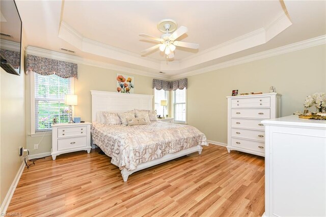 bedroom featuring a tray ceiling, light wood-type flooring, crown molding, baseboards, and ceiling fan