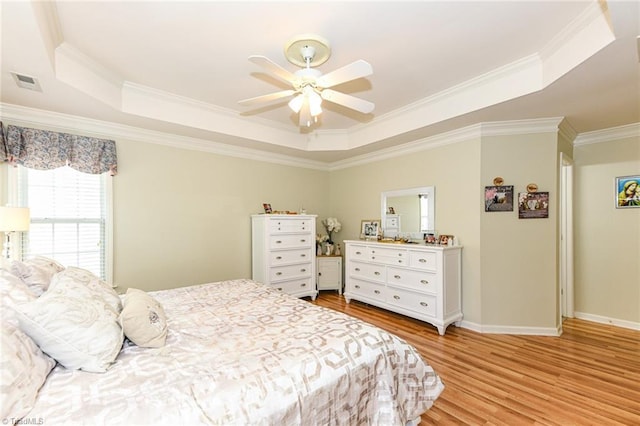 bedroom featuring a tray ceiling, crown molding, light wood-type flooring, a ceiling fan, and baseboards