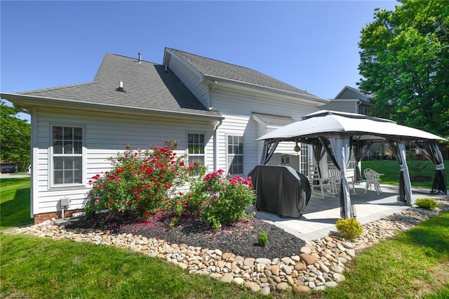 back of property featuring a gazebo, roof with shingles, a lawn, and a patio area